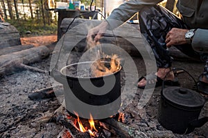 Man cooking in bowlers over a fire in the forest.