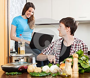 Man cooking food while girlfriend looking at laptop