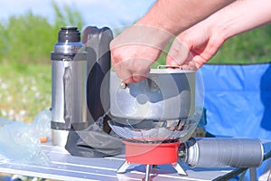 Man is cooking food using small gas burner in camping on nature, hands closeup.