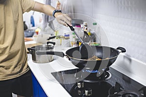 Man cooking fried chicken in kitchen of home He holds spatula and pan. with gas stove that is frying thai food for family