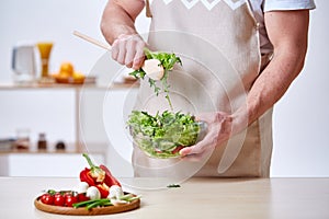 Man cooking at kitchen making healthy vegetable salad, close-up, selective focus.