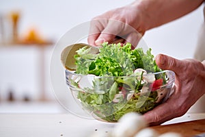 Man cooking at kitchen making healthy vegetable salad, close-up, selective focus.