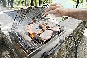 Man cooking meat at barbecue - Chef grilling meat in park outdoor near lake - Concept of eating bbq outdoor with gas grill during