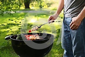 Man cooking sausages and vegetables on barbecue grill outdoors