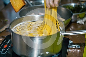 MAN COOKING SPAGHETTI PASTA IN PAN OF BOILING WATER ON COOKER HOB