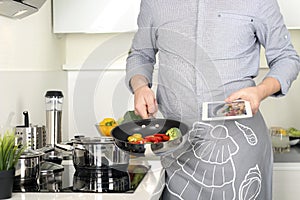 Man is cooking vegetables and using a tablet photo