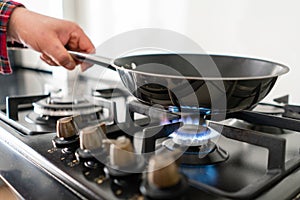 A man cooks in a frying pan, puts it on the stove. Modern gas burner and hob on a kitchen range. Dark black color and