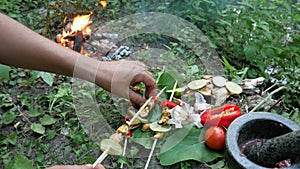 A man cooks mussels over a fire in the forest.
