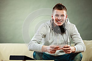 Man on couch with headphones smartphone and tablet