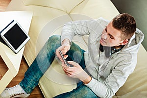 Man on couch with headphones smartphone and tablet