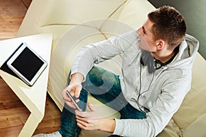 Man on couch with headphones smartphone and tablet