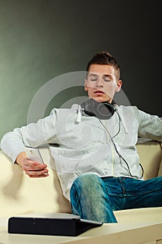 Man on couch with headphones smartphone and tablet