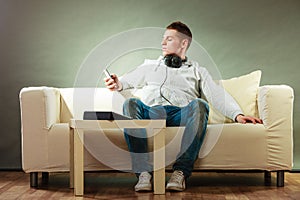 Man on couch with headphones smartphone and tablet