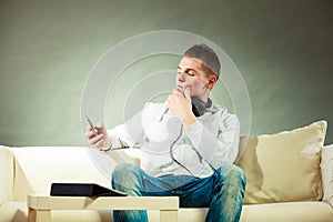 Man on couch with headphones smartphone and tablet