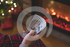 Man counting american dollars sitting near christmas tree and fireplace. Spending money on gift at christmas time. concept.