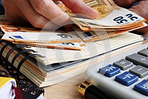 Man counting euro banknotes. Desk with calculator, ledger and euros.