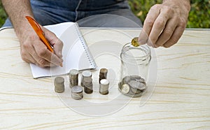 A man counts small coins and writes them down in a notebook. Concept of poverty, pension, savings