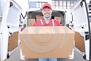 Man courier holds cardboard box on background of car