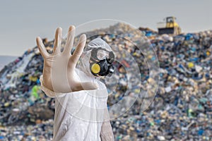 Man in coveralls is showing stop gesture. Garbage pile in landfill in background photo