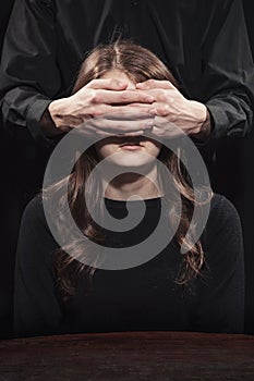 Man covered his eyes with a young woman on a black background