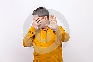 Man covering eyes and raising hand to stop, feeling stressed afraid, refusing to watch scary content