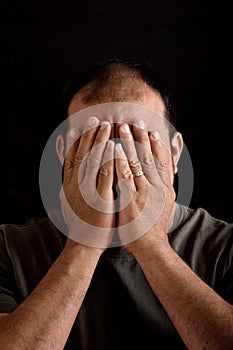 Man covering his face on black