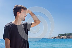 Man covering his face with hand from sunlight and looking at sea coast