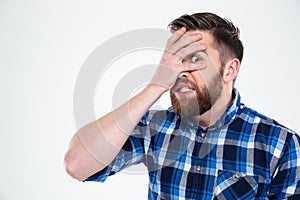 Man covering his face with palm and looking at camera through fingers