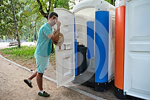 Man covering his nose while is opening the door of a smelly portable toilet.