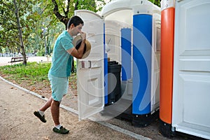 Man covering his nose while is opening the door of a smelly portable toilet.