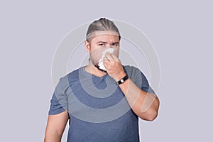 A man covering his nose with a piece of tissue paper. Suffering from a runny nose