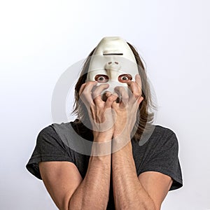 A man covers his face with a white mask upside down and tries to tear it off. The concept of personality crisis, fear, paranoia or