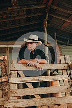 a man in cowboy clothes leaning on a fence and staring off to the left