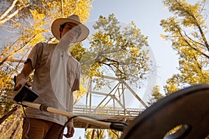 Man in a cowboy hat uses a metal detector to look for buried treasure in the autumn season with changing foliage seen from a low-a