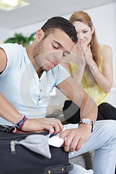 Man cramming clothes into suitcase girlfriend laughing