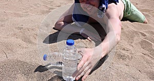 Man crawling on sand of desert and reaching for plastic water bottle 4k movie