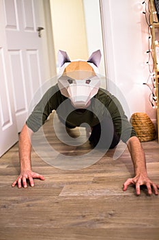 A man crawls on the ground wearing a fox mask