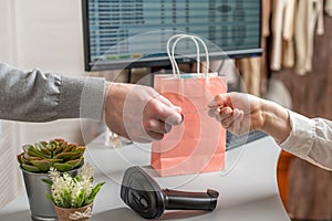 Man with credit card buying gift in a female clothing store. Woman cashier, seller scanning using barcode scanner at the checkout.