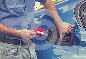 Man with credit card opening fuel tank of new car