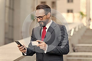 Man with credit card and smart phone outside of office. businessman making order with credit card by phone while walking. Business