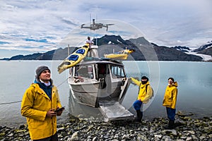 Man with crew members from scientific expedition  send a drone near the vessel docked on iceberg rock bay at wintertime to explore