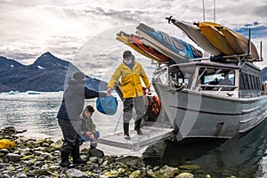 Man with crew members from scientific expedition unload the vessel docked on iceberg rock bay at wintertime to explore the island