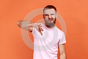 Man criticizing bad quality with thumbs down displeased grimace, showing dislike gesture.