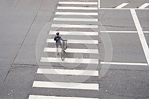 Man crosses the road at a pedestrian crossing and carries a bicycle next to him. View from above.