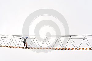 Man crossing rope bridge over the abyss in foggy mountains