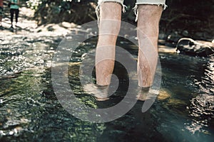 Man crossing the small mountain river bare feet on hiking trail.