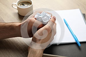 Man crumpling paper on wood table with copybook and cup of coffee