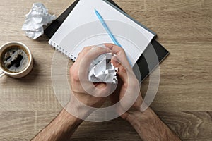 Man crumpling paper on wood table with copybook and cup of coffee