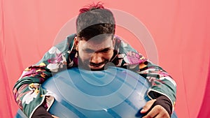 Man crying depressed in floral shirt with exercise ball on red background