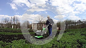 Man cultivates the ground in the garden with a tiller, preparing the soil for sowing